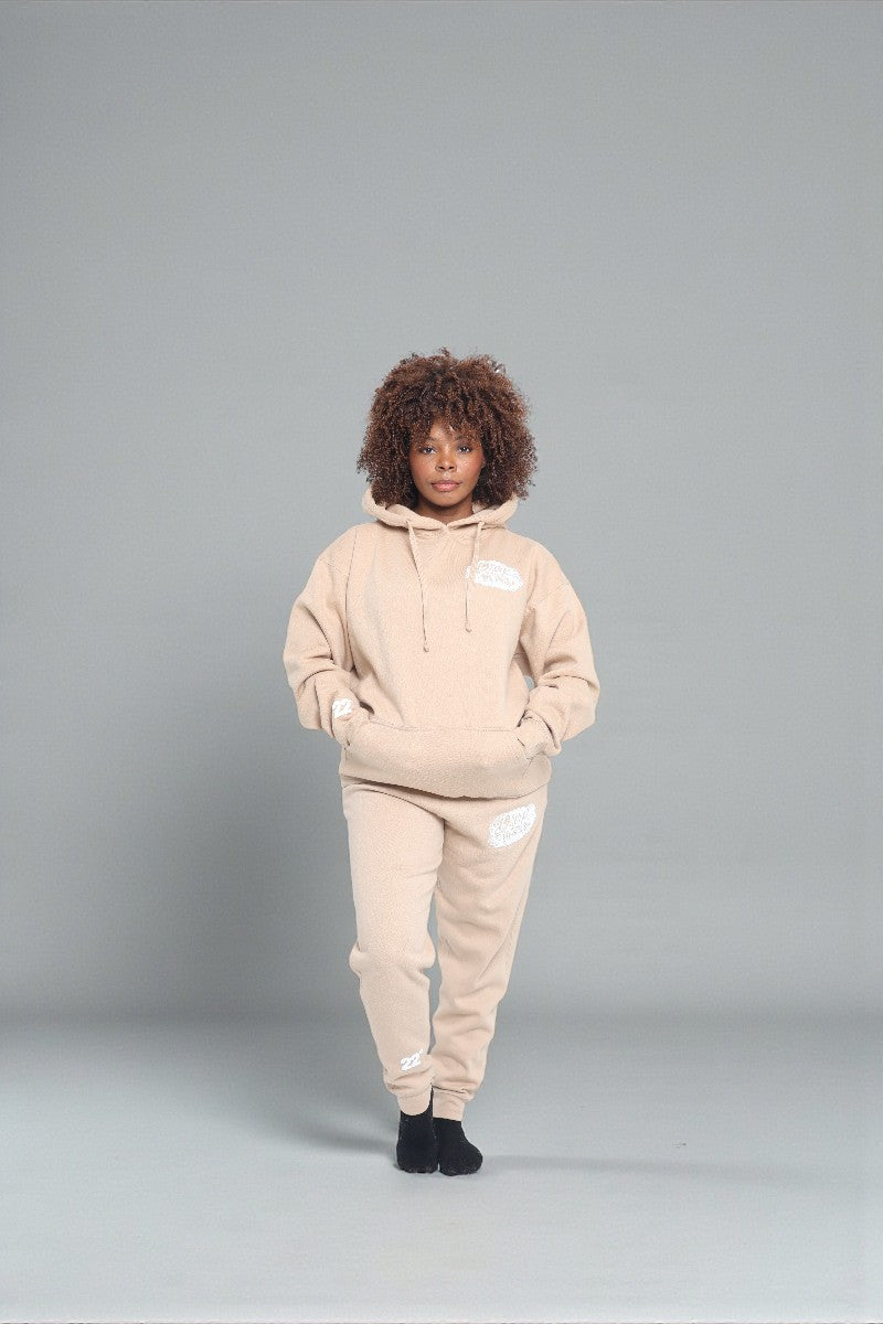 Person wearing a beige hoodie and pants set on a gray background